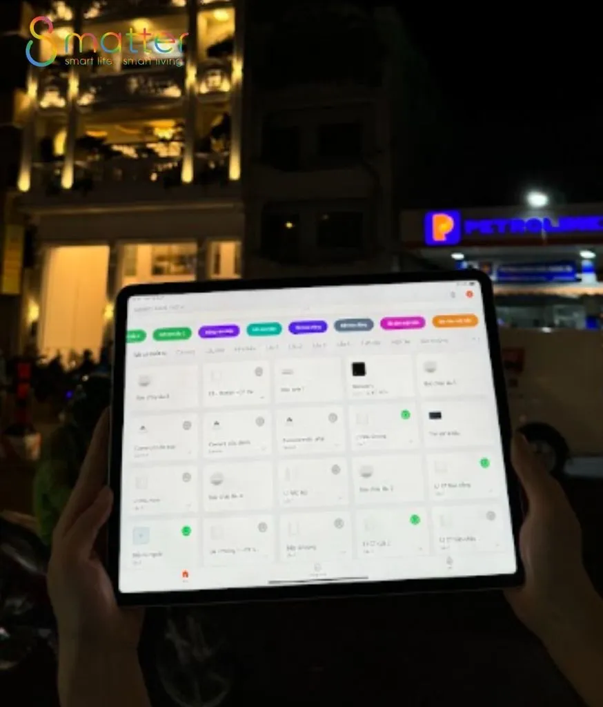 Hai tay cầm iPad mở app điều khiển nhà thông minh ban đêm