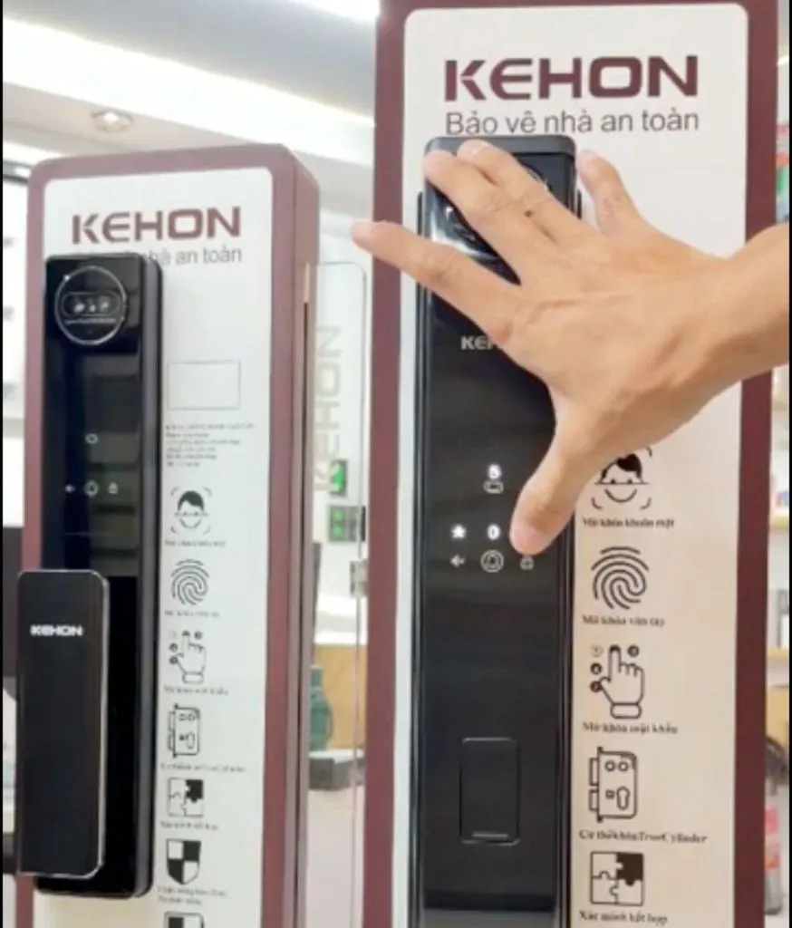 Bàn tay đưa gần một khóa trưng bày trong cửa hàng, cạnh bảng hiệu KEHON