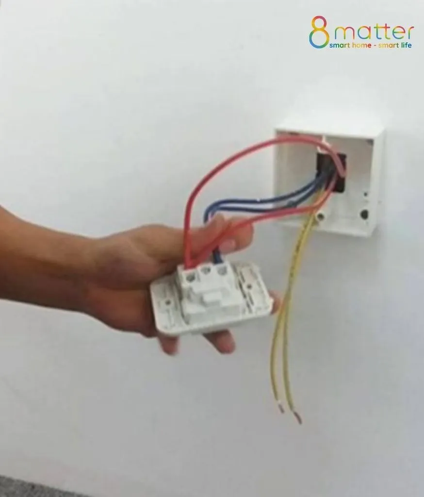 Bàn tay cầm mặt công tắc đang đấu dây đỏ xanh vào đế âm