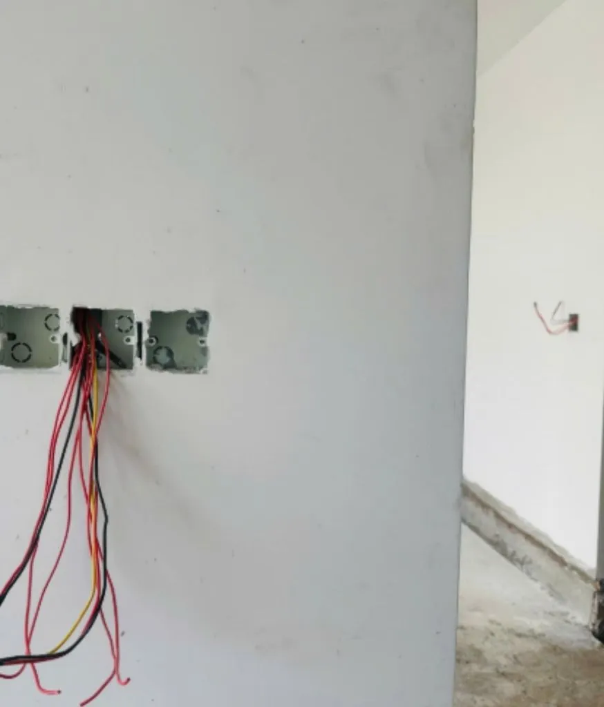 Tường trắng có ba đế âm công tắc và bó dây điện thò ra