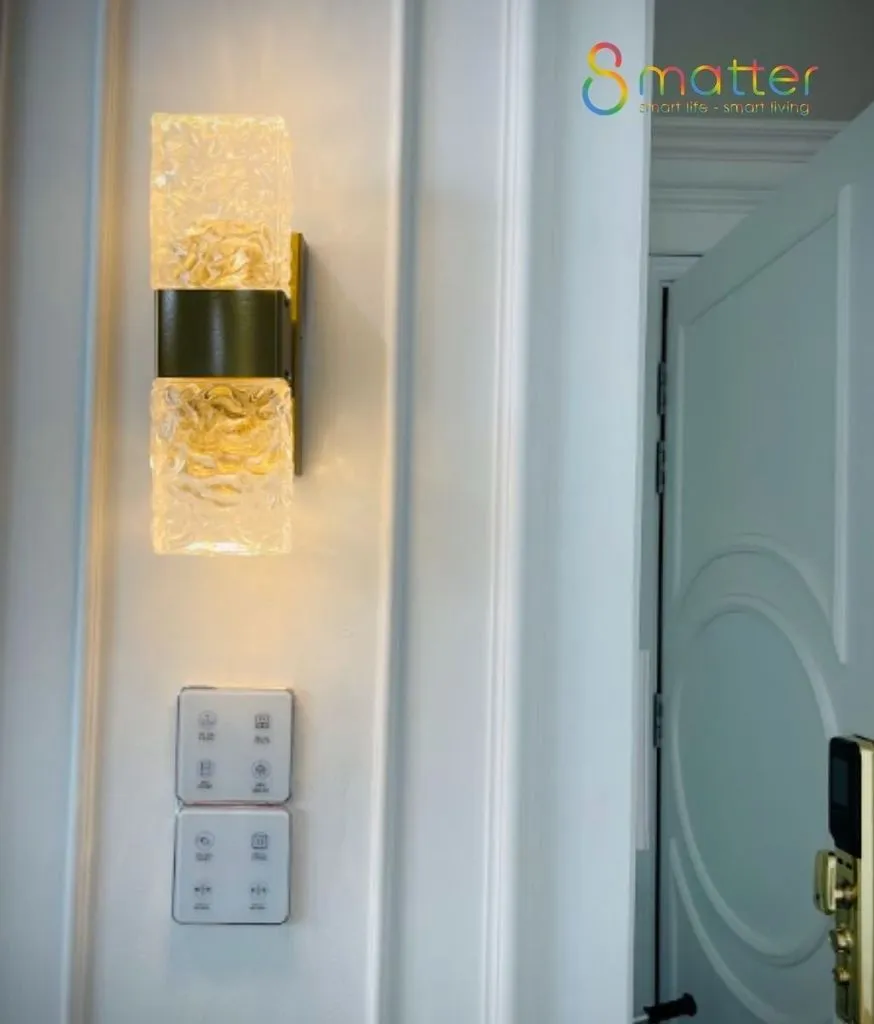 Đèn tường pha lê vàng bên cạnh cửa, phía dưới gắn bộ công tắc cảm ứng trắng
