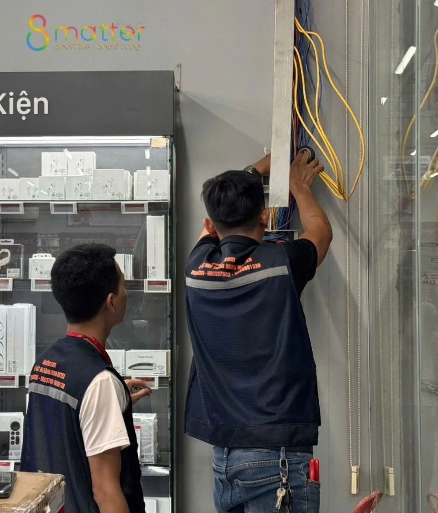 Hai kỹ thuật viên đồng phục lắp thiết bị lên cột trong cửa hàng