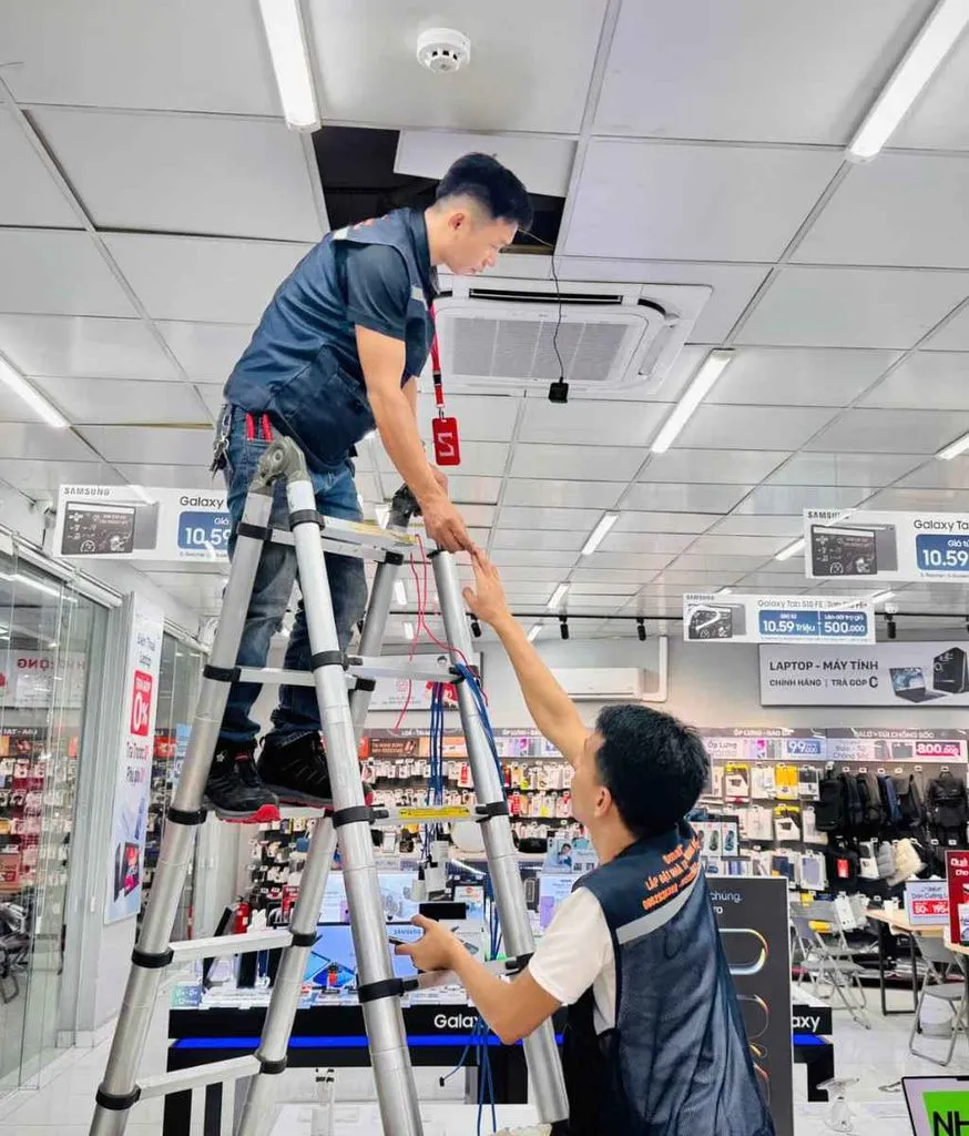 Hai kỹ thuật viên đứng trên thang, lắp thiết bị lên trần của một cửa hàng