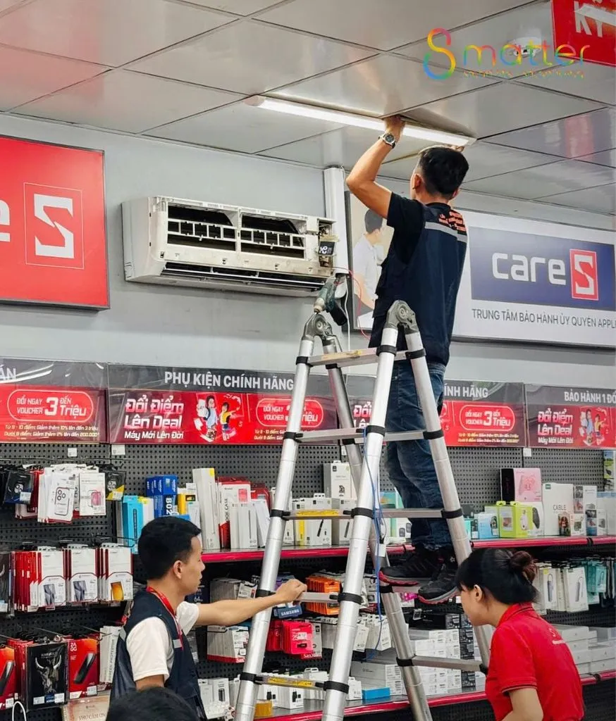 Hai nhân viên cùng nâng và lắp một dàn lạnh điều hoà trong cửa hàng