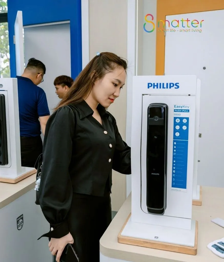 Khách nữ đang xem khóa Philips trưng bày trong cửa hàng, phía sau có nhân viên
