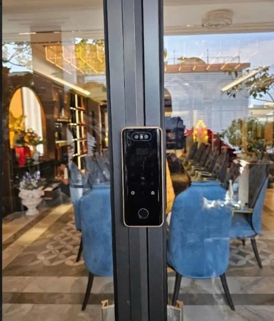 Khoá có camera trên cửa nhôm đen, nhìn vào nhà hàng ghế bọc xanh sang