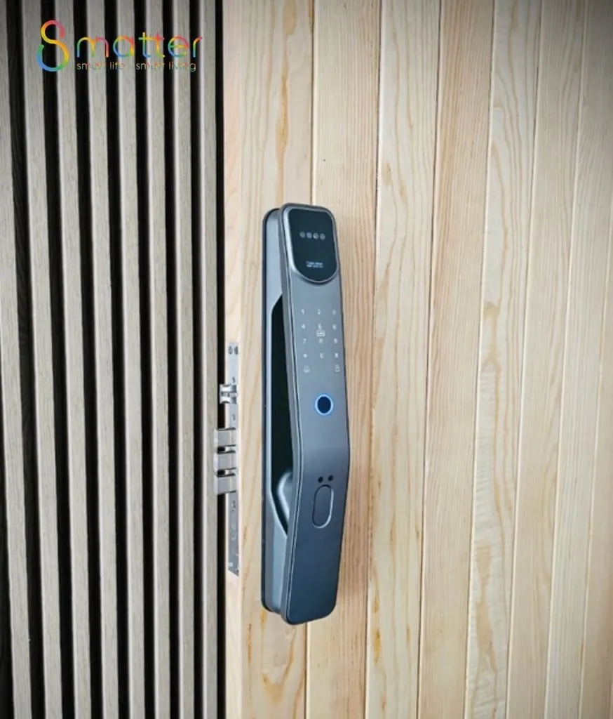 Khoá cửa đẩy màu xám than gắn trên cánh cửa gỗ sáng, nền vách lam