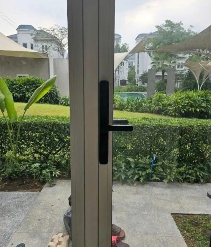 Cửa nhôm kính lắp khoá đen, phía ngoài là sân cỏ và căn biệt thự