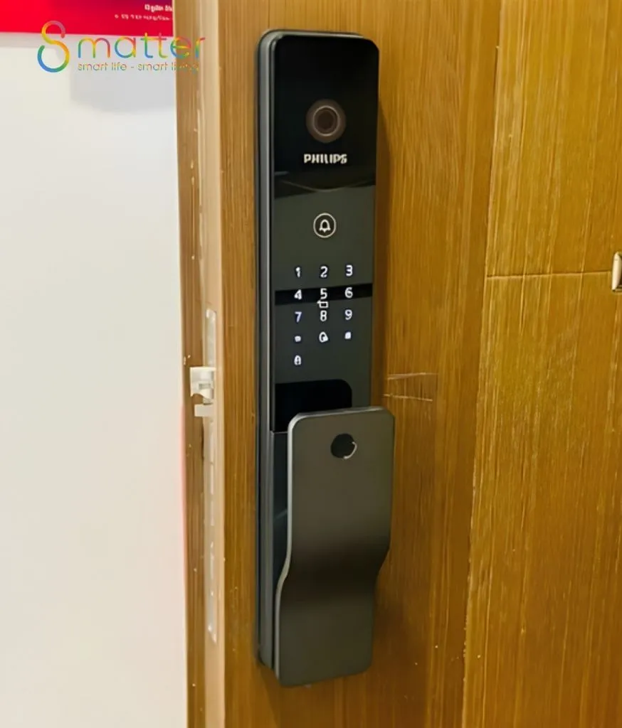 Khoá cửa vân tay Philips đen trên cánh cửa gỗ vàng, có camera và bàn phím
