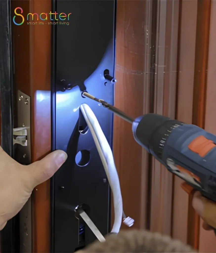 Bàn tay giữ cánh cửa gỗ đã khoét lỗ, tay kia dùng máy khoan luồn dây