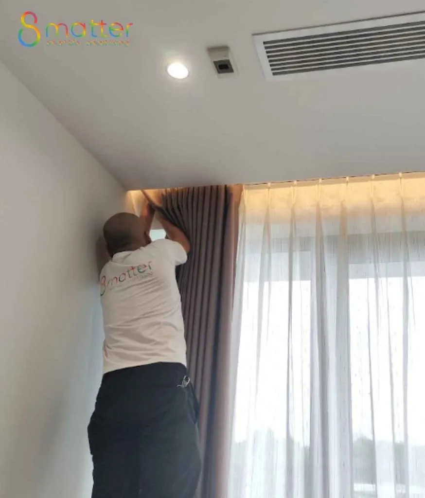 Kỹ thuật viên lắp thiết bị trên trần nhà cạnh cửa sổ và rèm