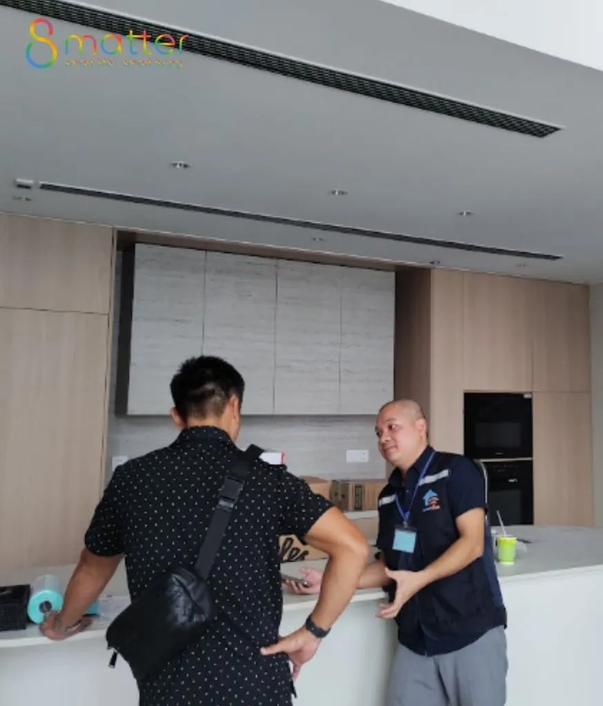 Hai người đứng nói chuyện bên đảo bếp trắng, nhân viên áo xanh đeo thẻ