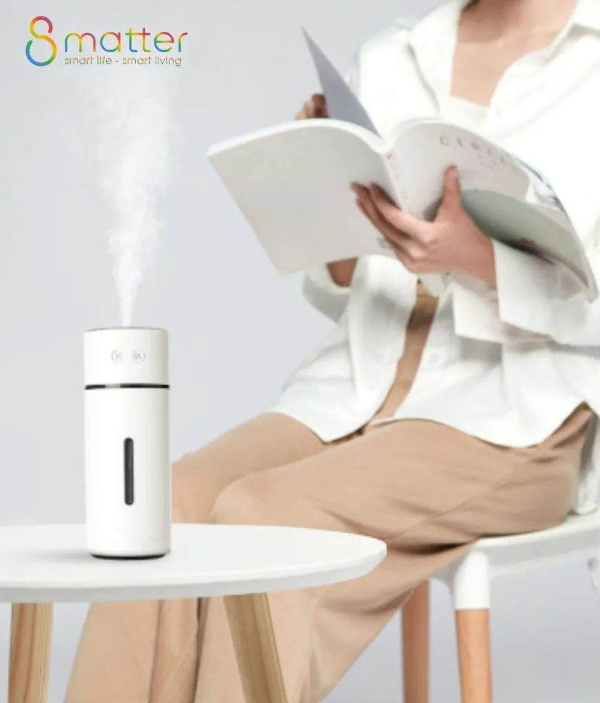 Người phụ nữ ngồi đọc sách cạnh máy tạo ẩm đang phun sương trên bàn