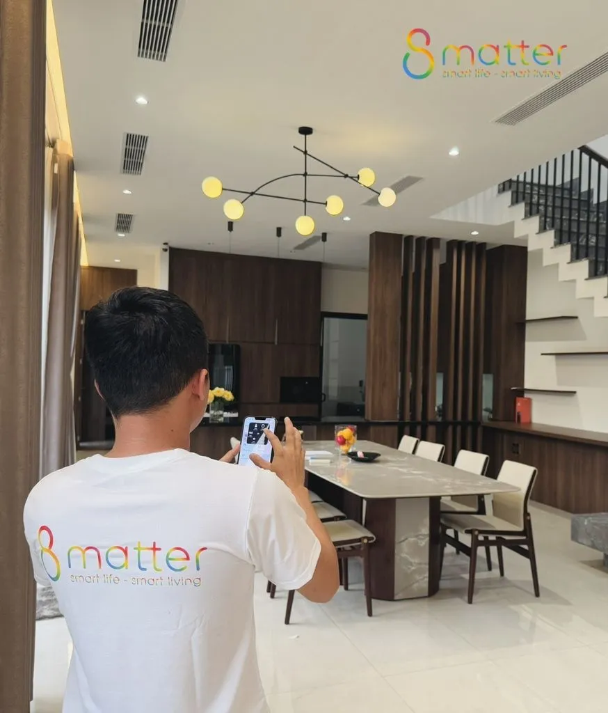 Người đứng trong phòng khách cầm điện thoại xem hình ảnh từ camera