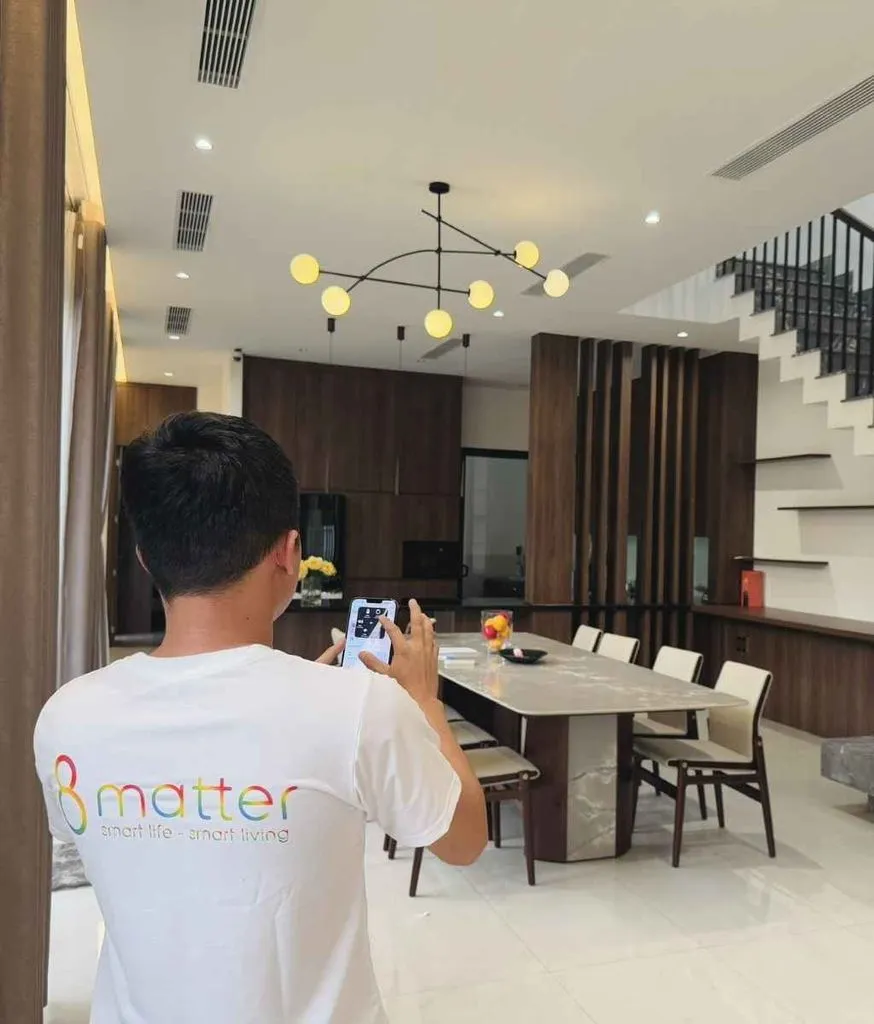 Người mặc áo 8matter giơ điện thoại lên trong phòng ăn của một căn nhà