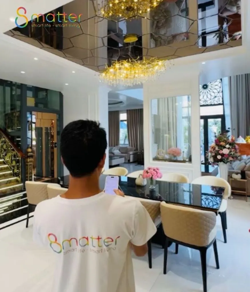 Nhân viên mặc áo 8matter đứng trong phòng khách biệt thự có cầu thang và đèn chùm