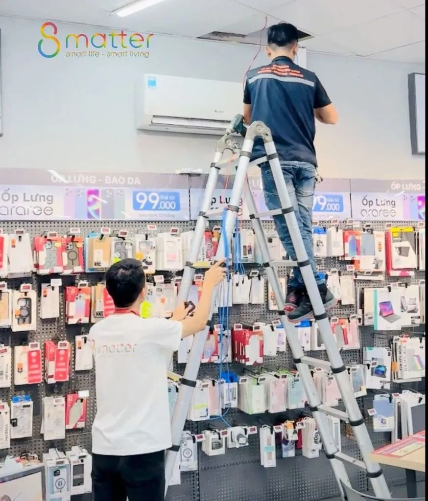 Nhân viên đứng trên thang lắp thiết bị ở phía trên dãy kệ hàng