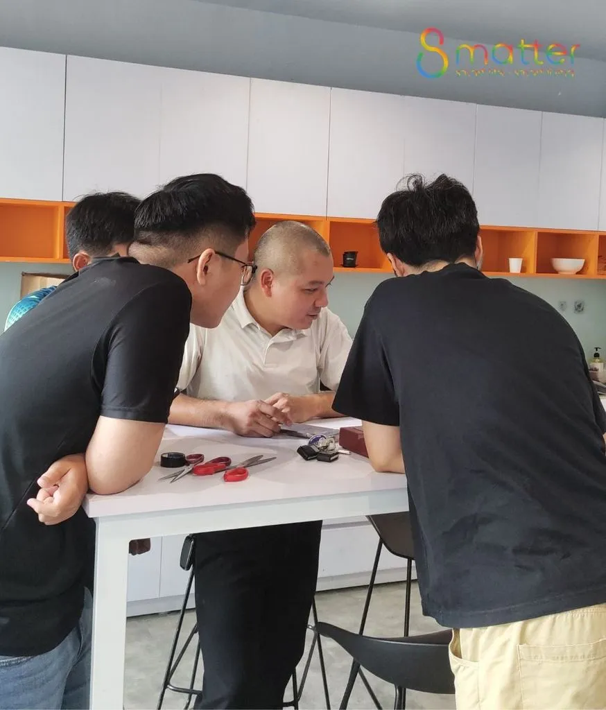 Nhóm nhân viên đứng quanh chiếc bàn, cùng xem các thiết bị đặt trên mặt bàn