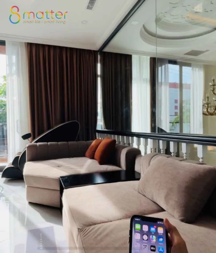 Phòng khách có sofa và rèm, bàn tay cầm điện thoại điều khiển