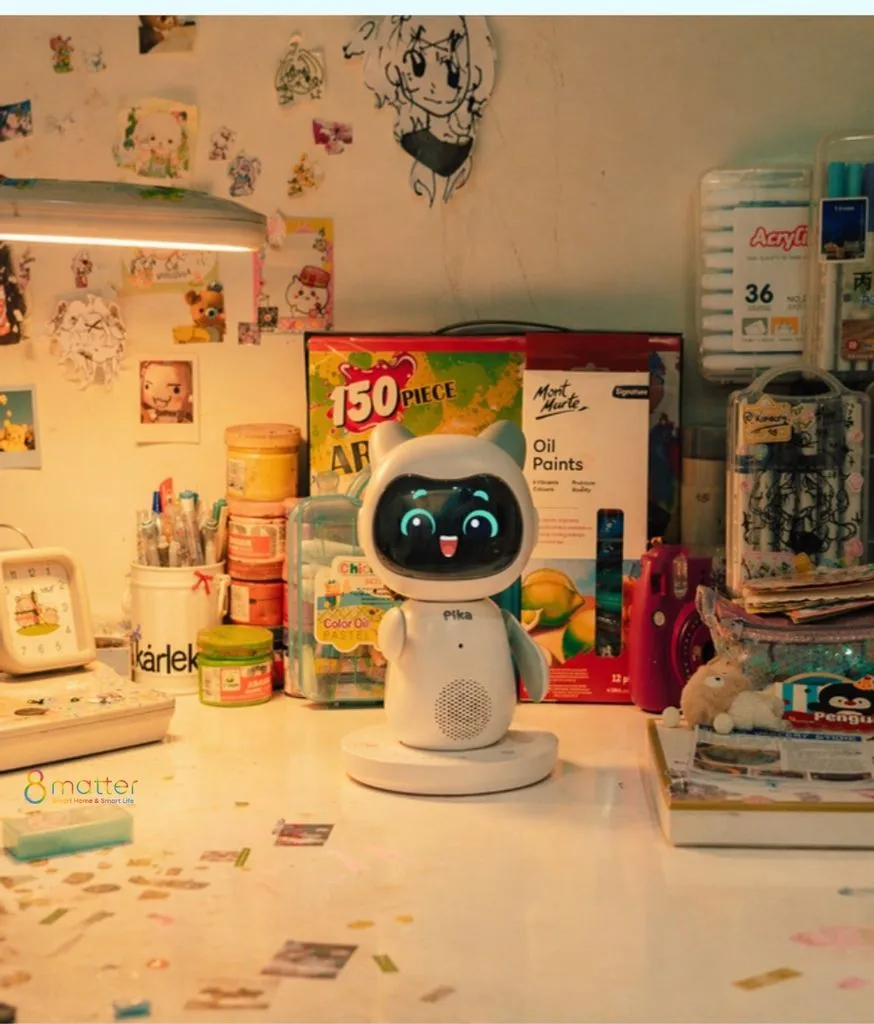Robot Pika đặt trên bàn học chất đầy hộp màu vẽ, bút và đồ dùng của bé