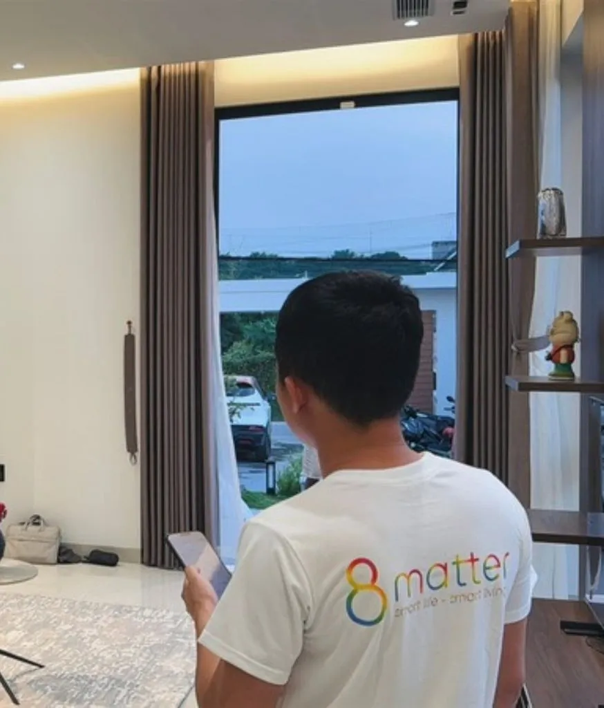 Kỹ thuật viên áo 8MATTER cầm điện thoại kiểm tra rèm tự động trước cửa kính lớn